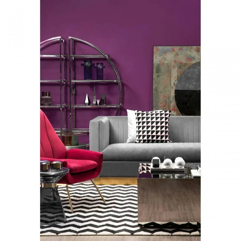 Grey velvet sofa with geometric cushions, red accent chair, black and white rug, chrome shelving