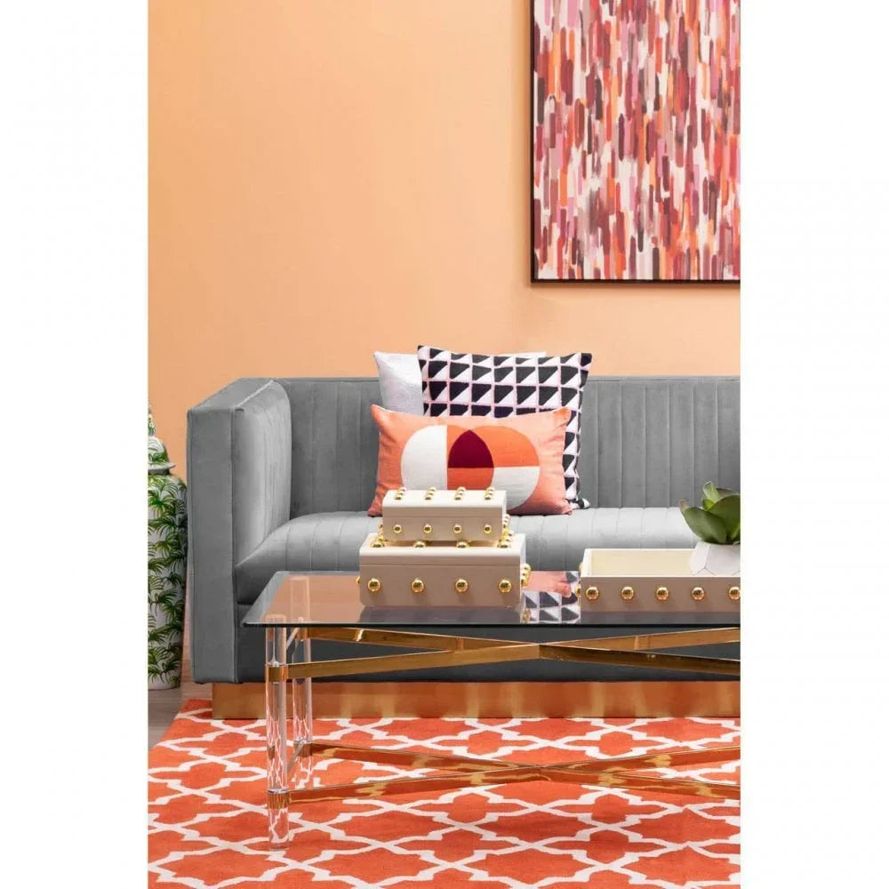 Grey velvet sofa with geometric cushions, glass coffee table, and orange patterned rug