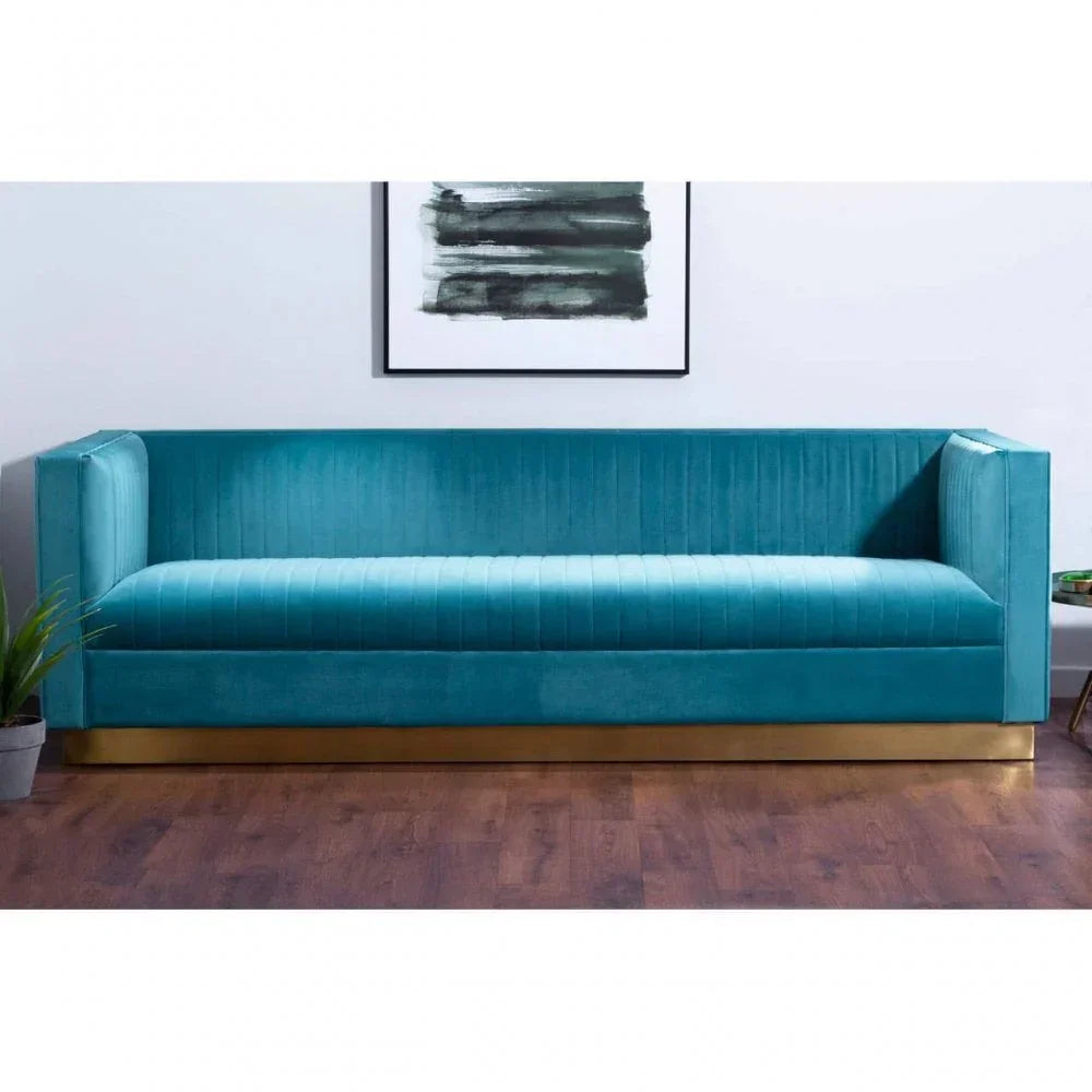Teal velvet sofa with gold base on wooden floor, modern wall art above, plant beside