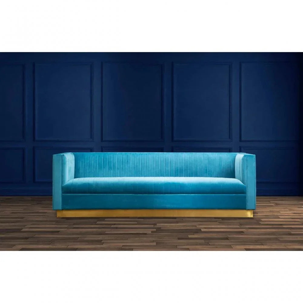 Turquoise velvet sofa with gold base on wooden floor against dark blue paneled wall