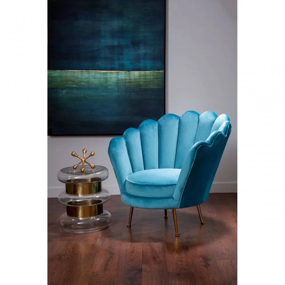 Blue velvet accent chair with scalloped back and gold legs beside clear and gold side table