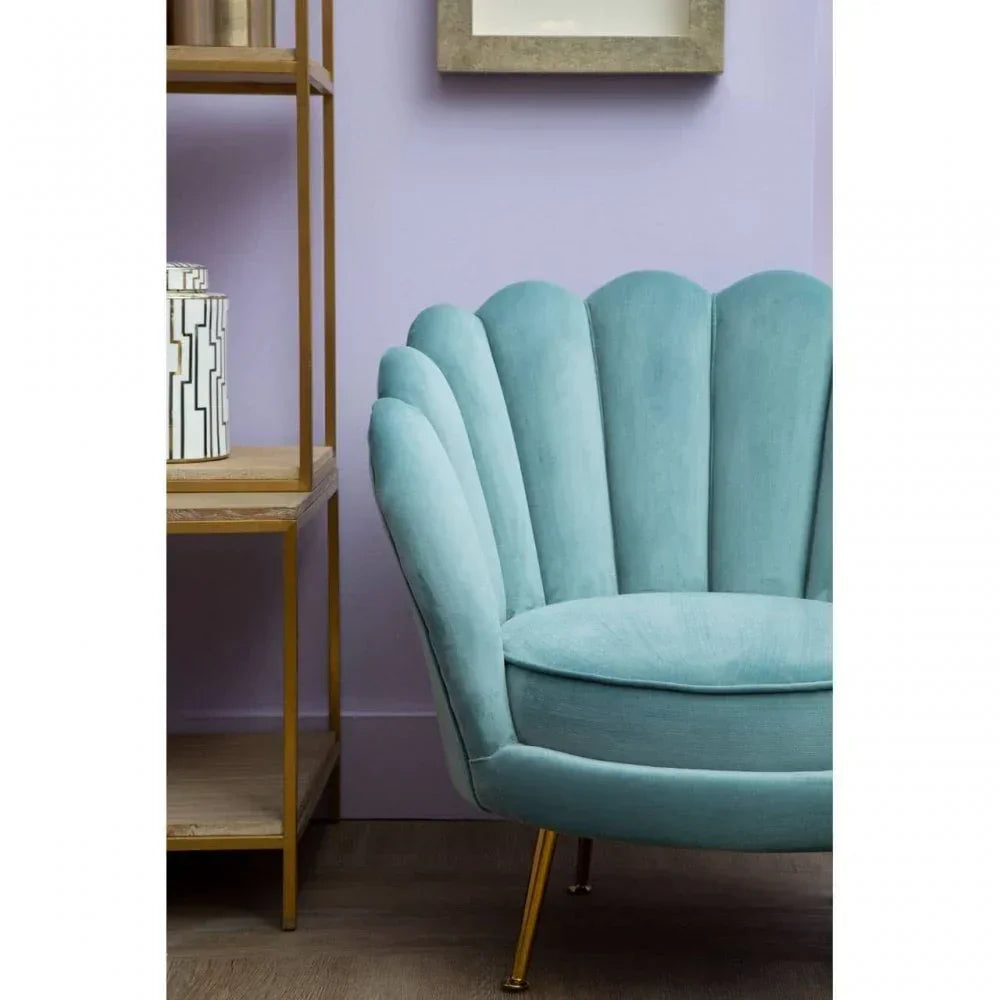 Velvet scallop accent chair in teal with gold legs beside wooden shelving on wood floor