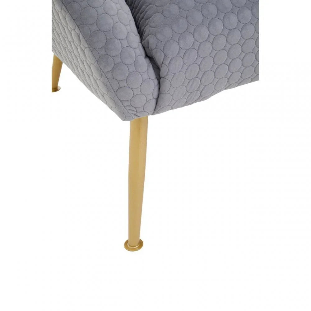 Grey upholstered chair with quilted circle pattern and gold metal legs close-up