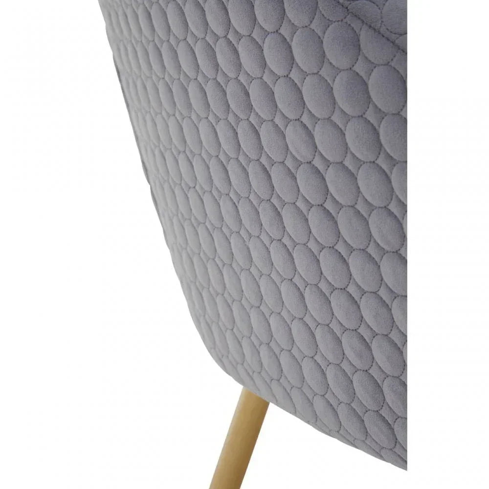 Close-up of grey quilted armchair upholstery with circular pattern and wooden leg