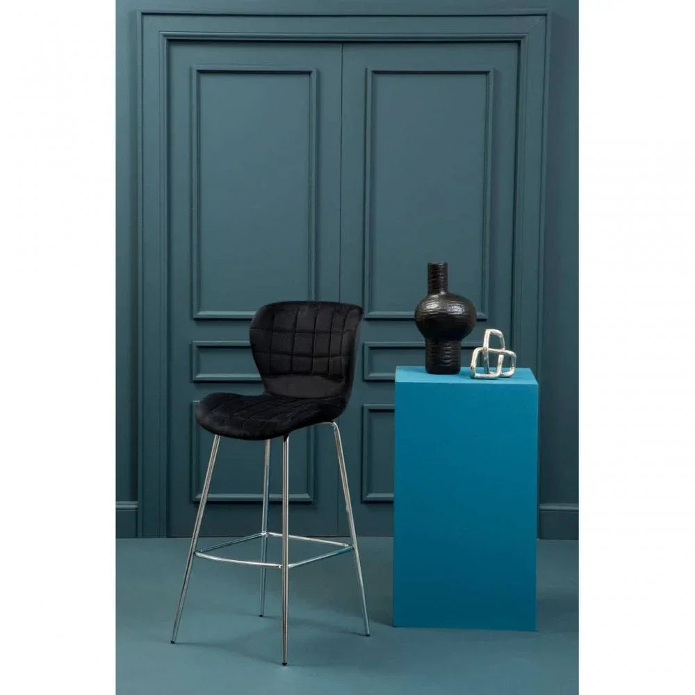 Black velvet bar stool with chrome legs beside blue pedestal and decorative vases