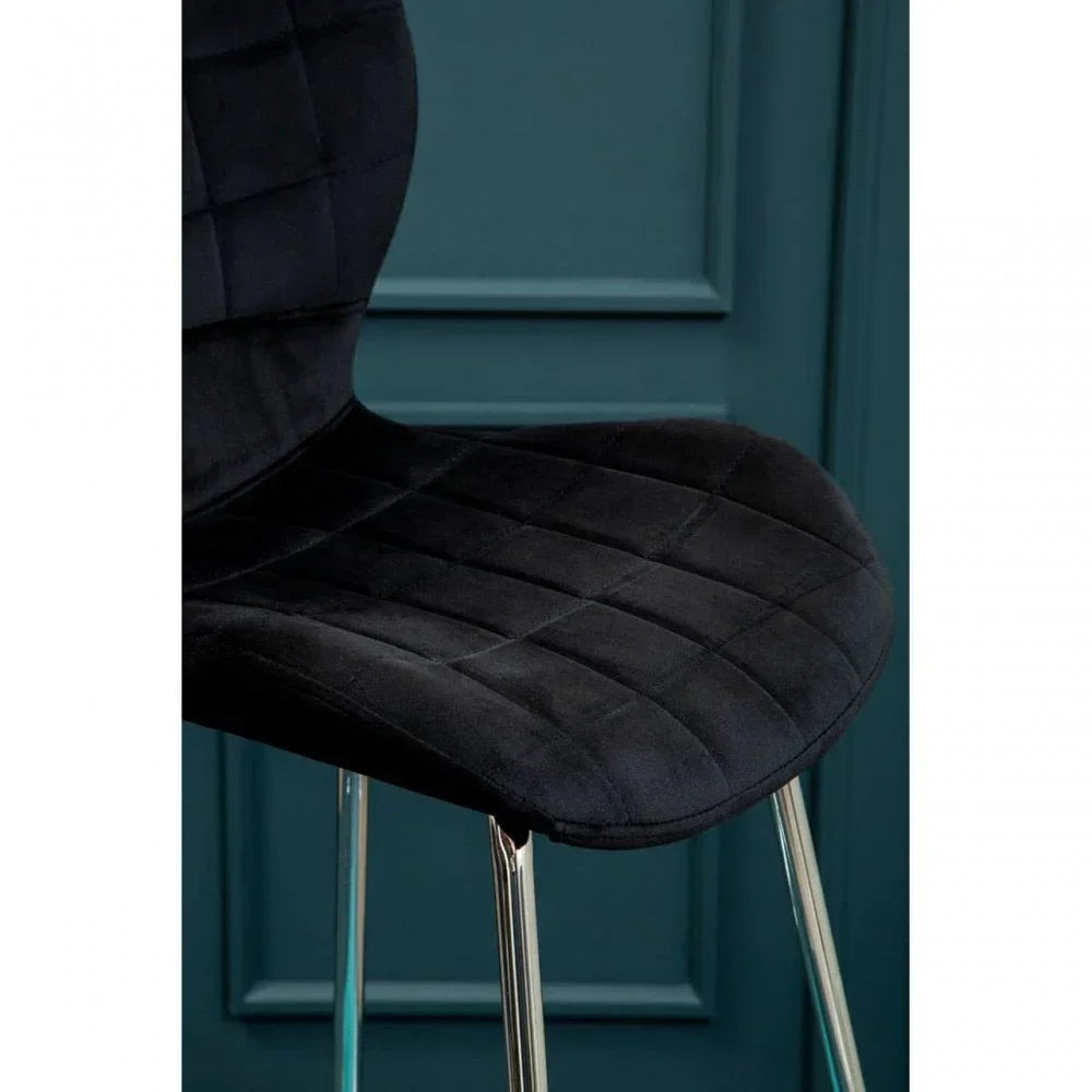 Black velvet dining chair with chrome legs against teal paneled wall