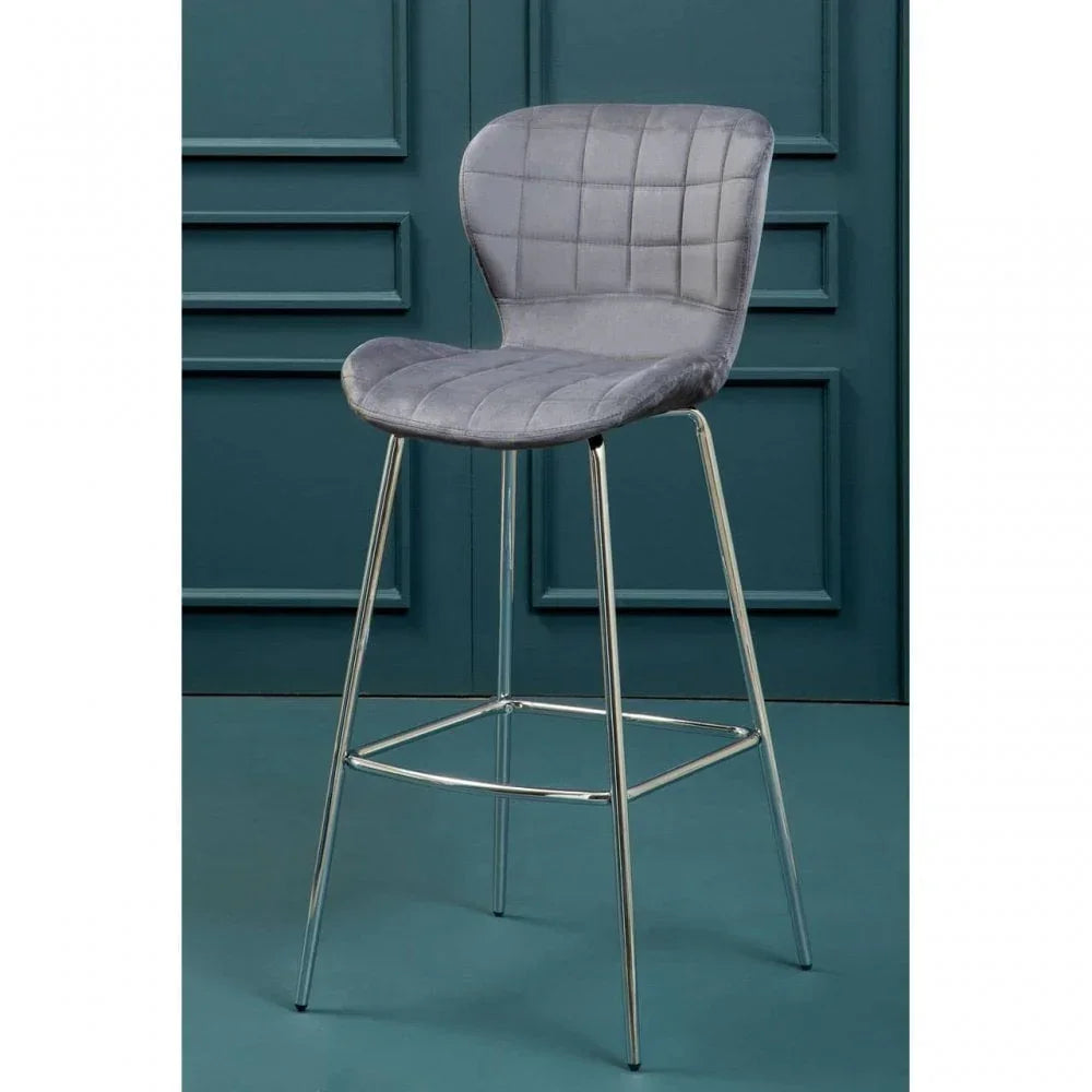 Grey velvet bar stool with quilted seat and chrome legs against teal paneled wall