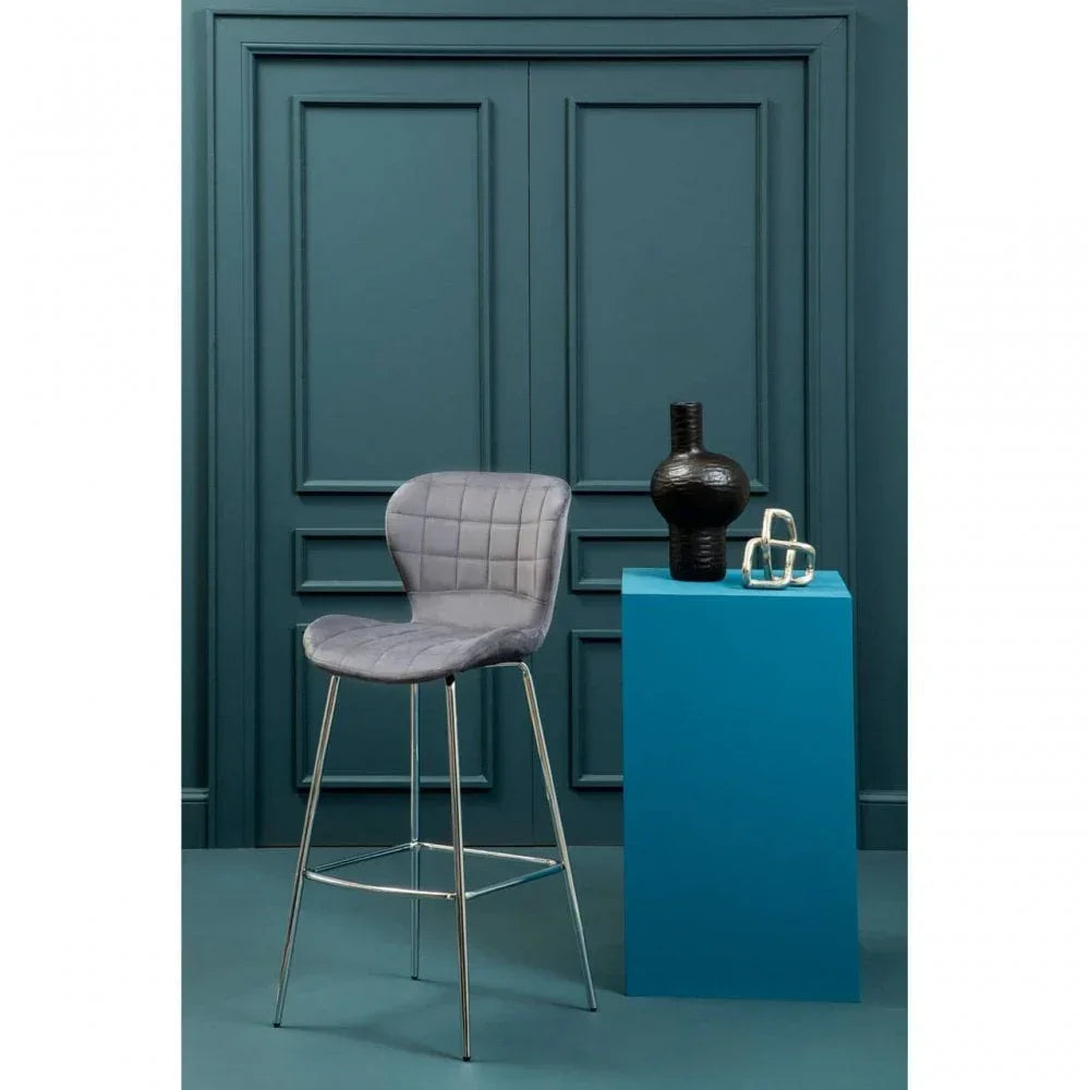 Grey upholstered bar stool with chrome legs beside blue pedestal and black vase