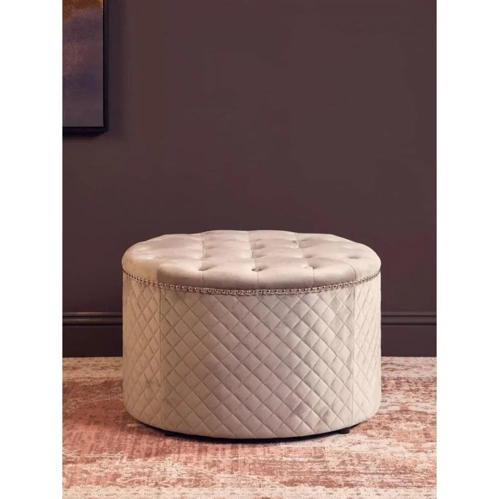 Round quilted velvet ottoman with button-tufted top and nailhead trim on carpeted floor