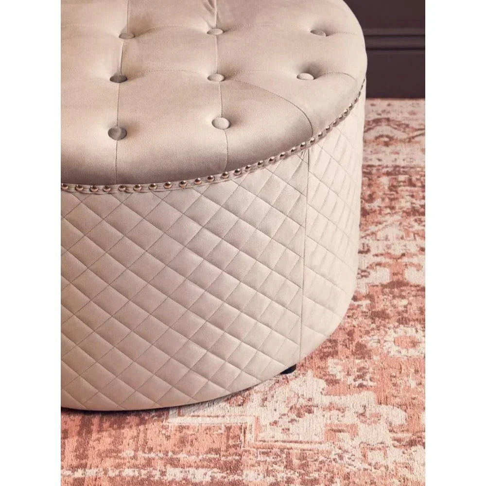 Beige quilted ottoman with button-tufted top and stud trim on patterned rug