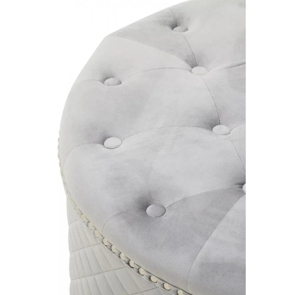 Close-up of grey velvet ottoman with button-tufted top and studded trim detail