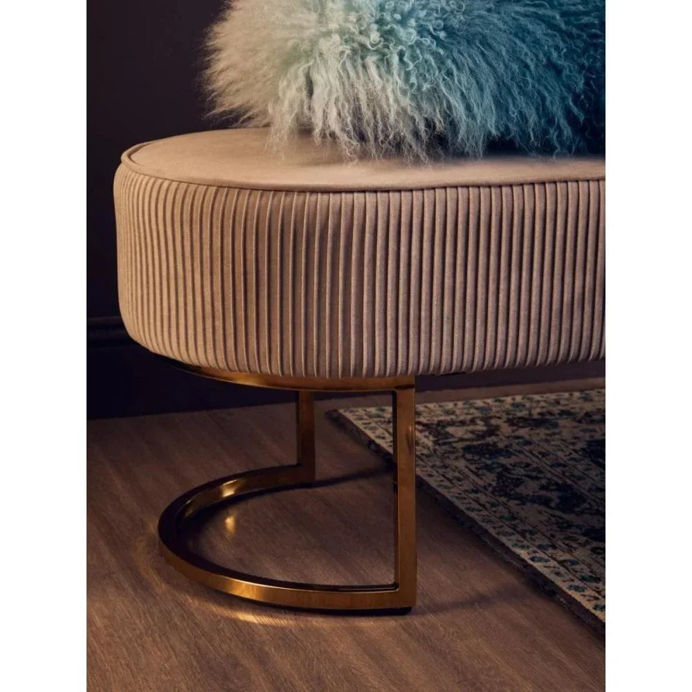 Velvet footstool with gold metal legs beside patterned rug on wooden floor