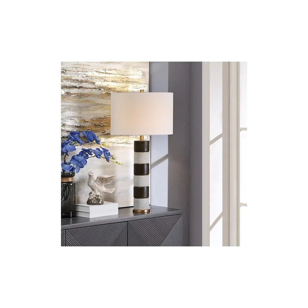 Striped ceramic table lamp with white shade on sideboard beside blue flowers and sculpture