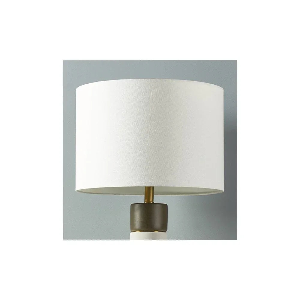 White fabric lampshade on table lamp with brass and black base against grey wall