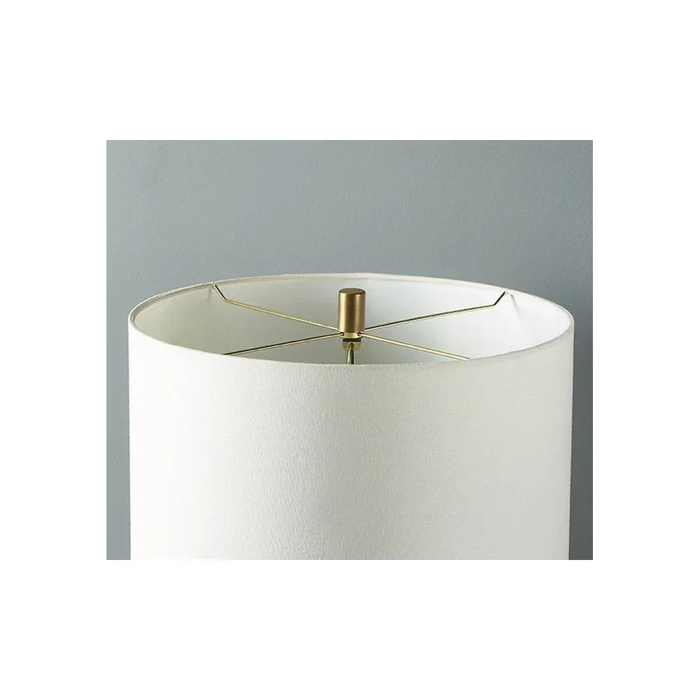 White fabric lampshade with gold metal frame against grey wall, close-up view