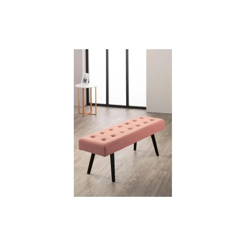 Pink upholstered bench with button tufting and black legs on wooden floor
