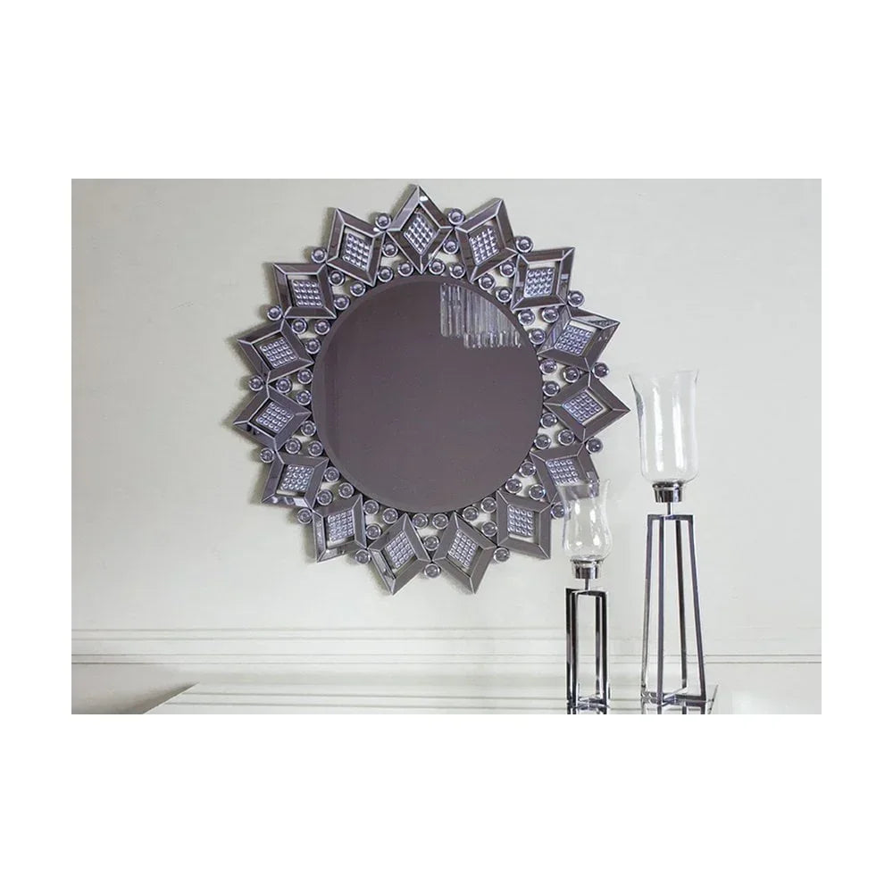 Round wall mirror with geometric silver frame above white console table and glass candle holders