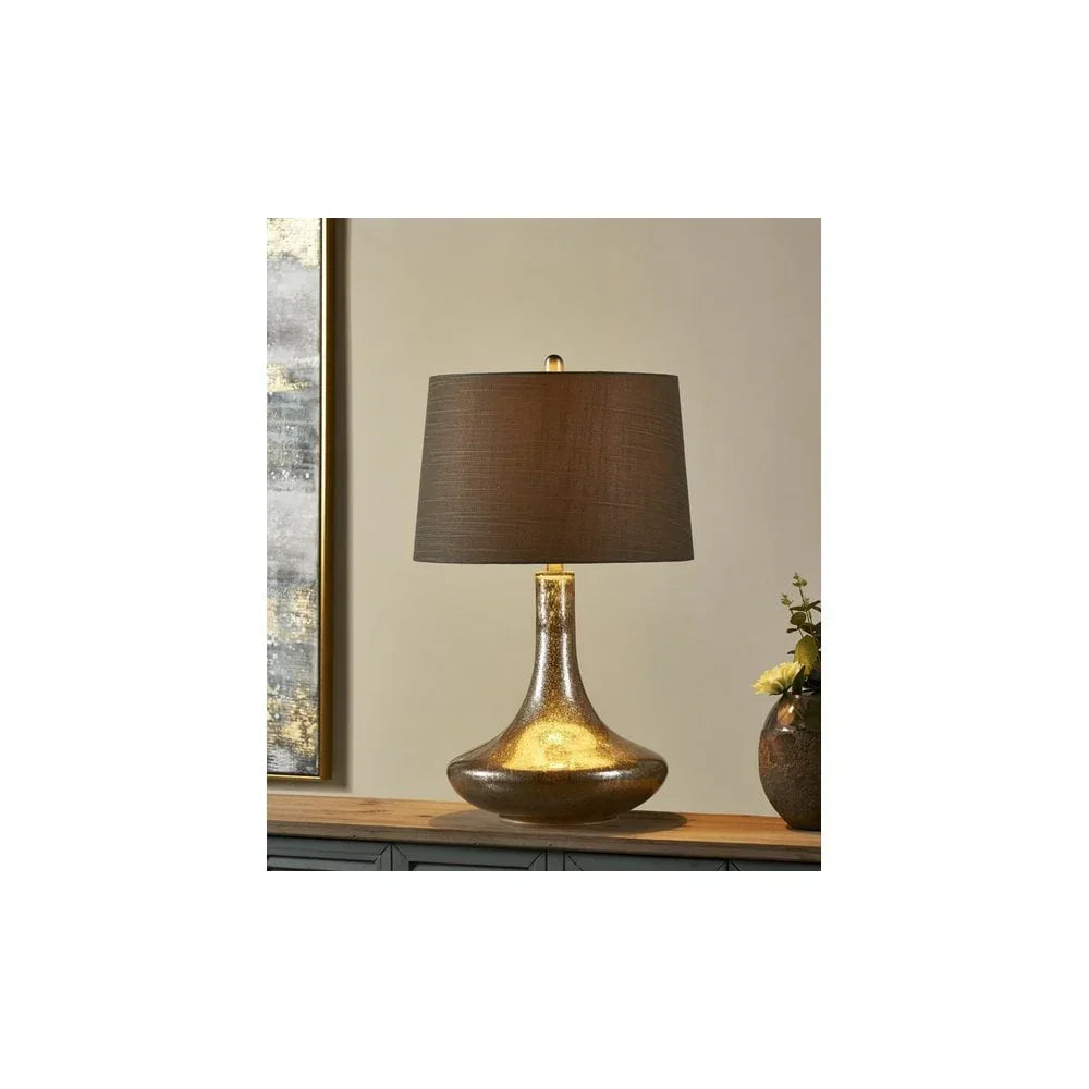 Gold glass table lamp with brown fabric shade on wooden sideboard