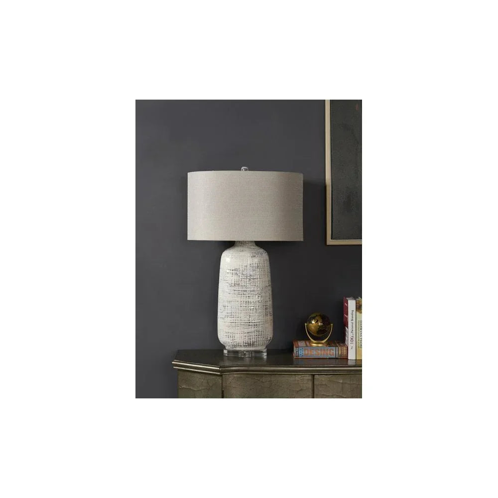 Ceramic table lamp with textured white base and grey shade on cabinet against dark wall