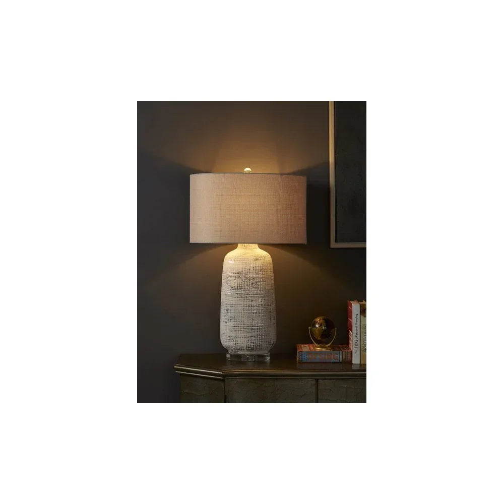 Textured ceramic table lamp with beige fabric shade on sideboard against dark wall