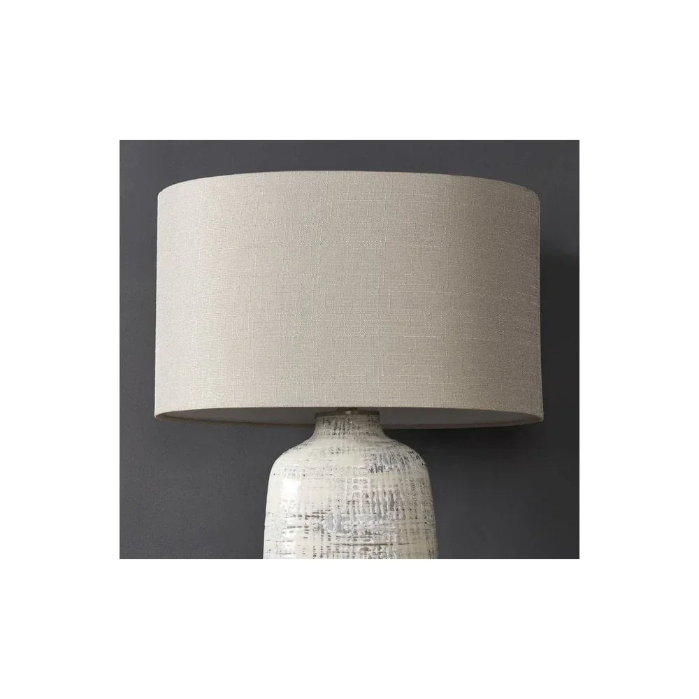 Beige fabric table lamp with textured ceramic base against dark wall