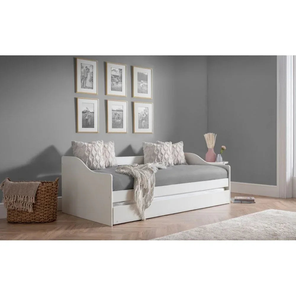 White wooden daybed with grey mattress, decorative cushions, and pull-out trundle drawer
