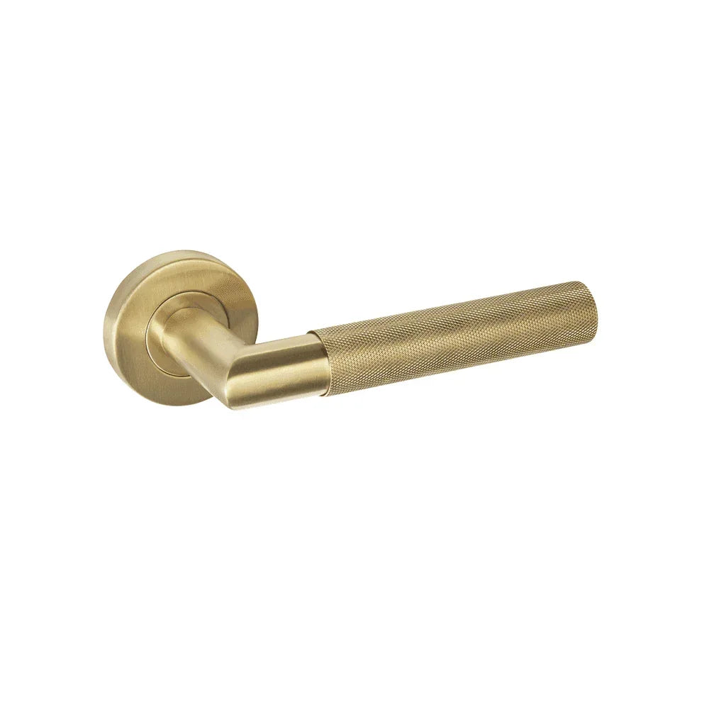 Brushed brass door handle with textured grip and round backplate on white background