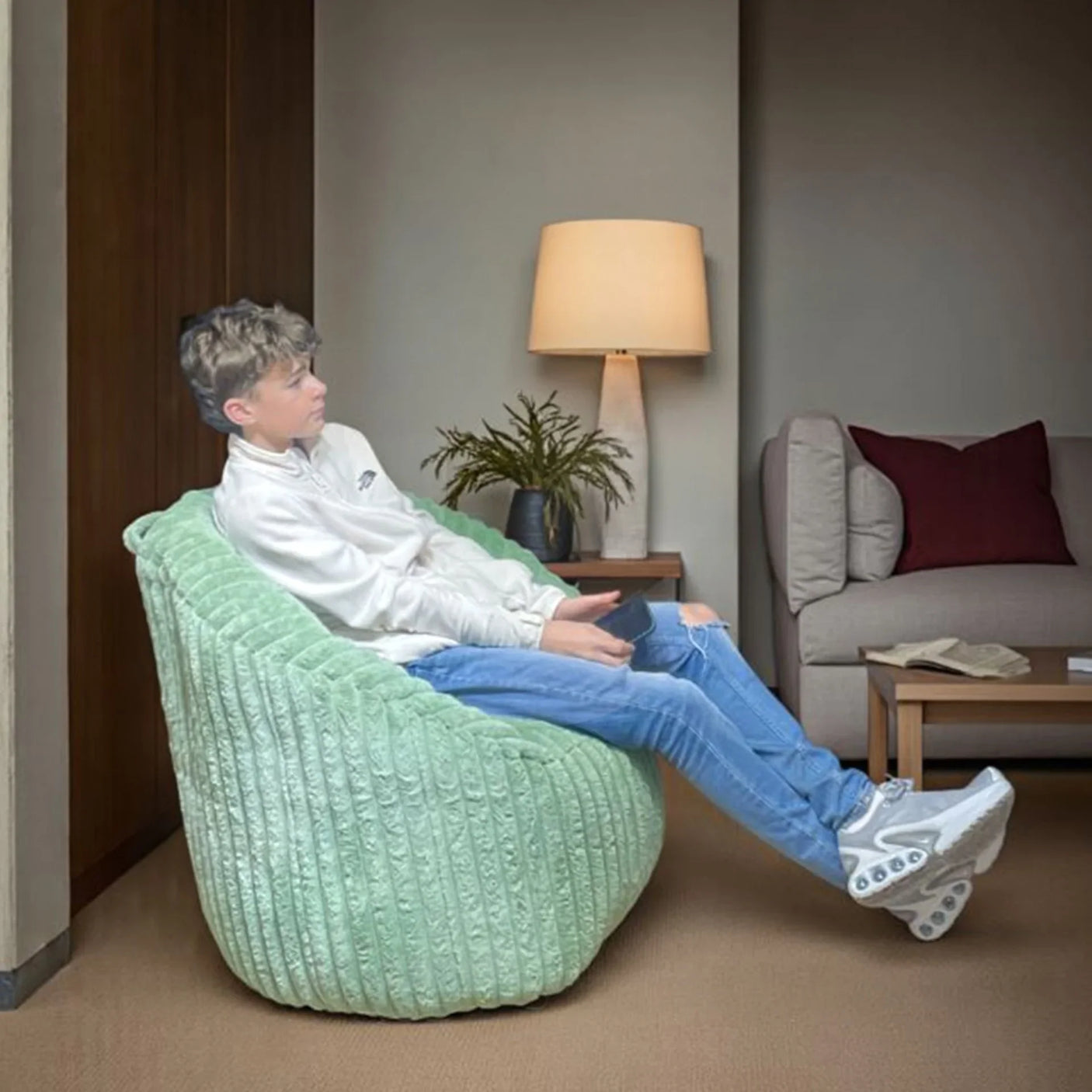 Green cord bean bag chair in lounge with person seated, next to lamp and coffee table