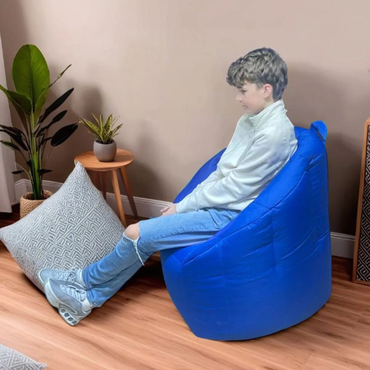 Blue Milano bean bag chair in living room with boy seated, wooden floor and plant nearby