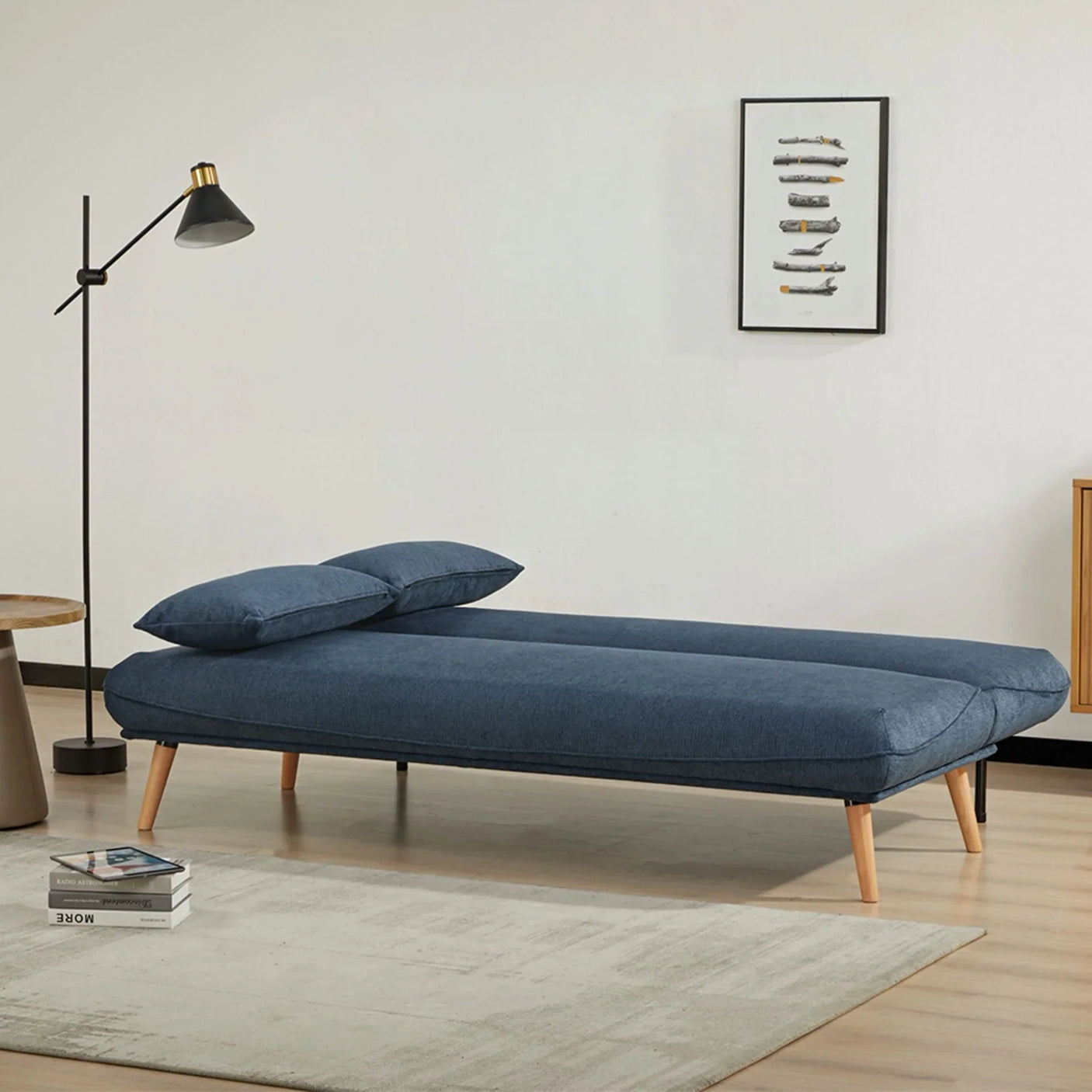 Blue fabric sofa bed with wooden legs styled in a modern living room setting