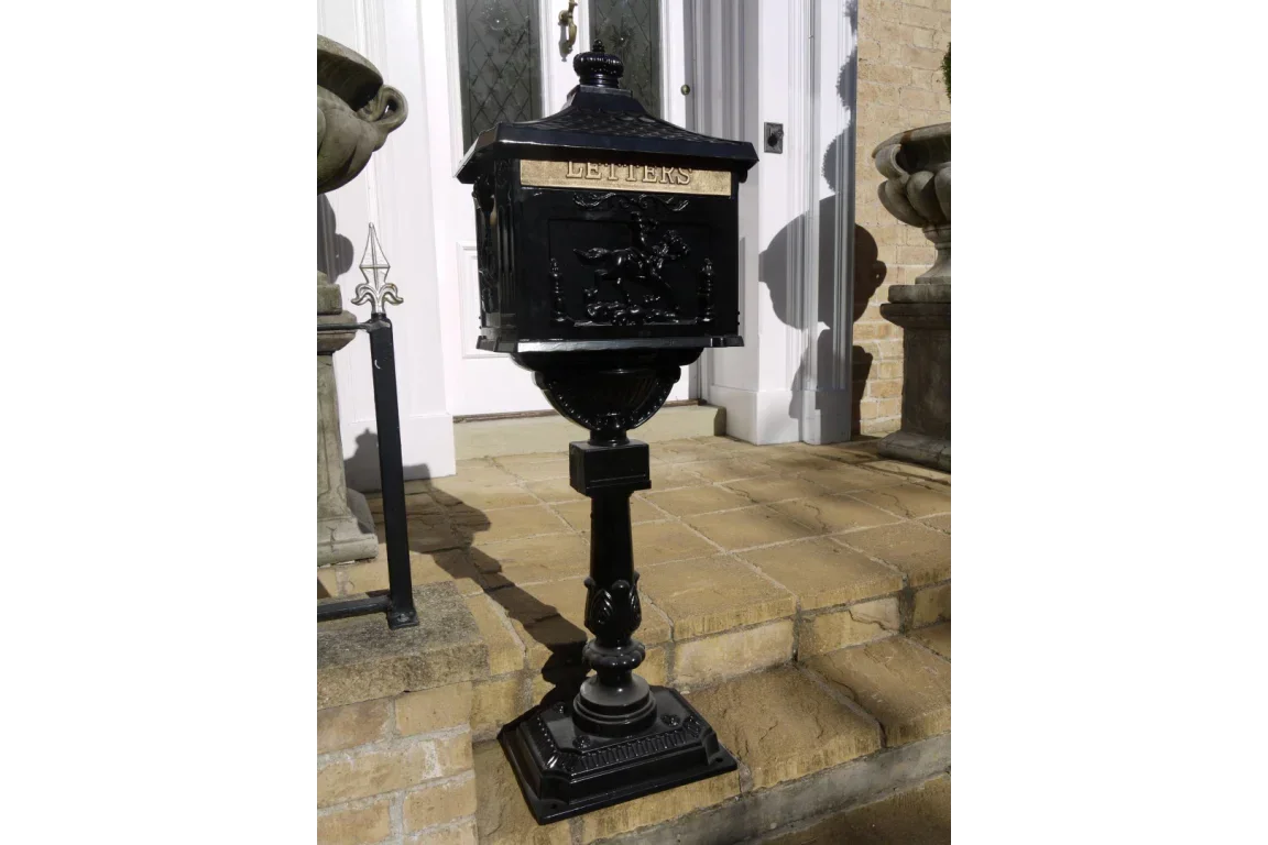 Black cast iron post box with gold lettering on pedestal by front door steps