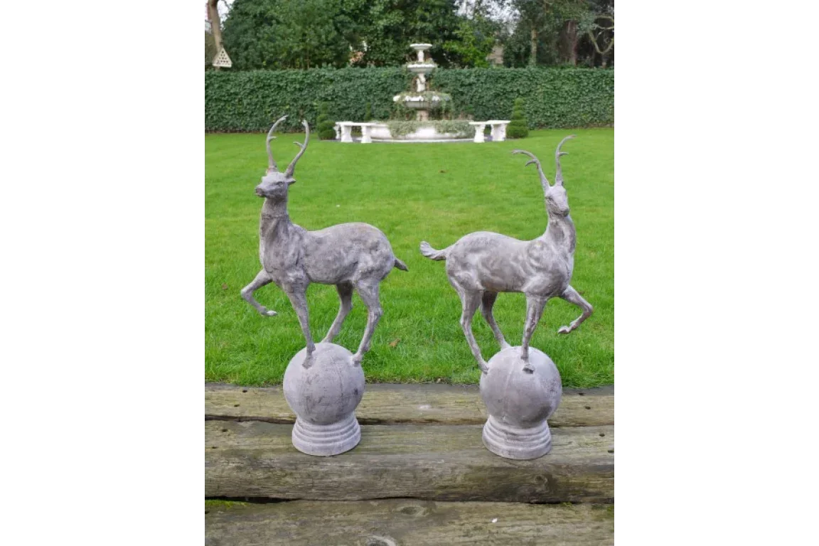 Pair of grey deer garden ornaments on plinths with grass lawn and fountain backdrop