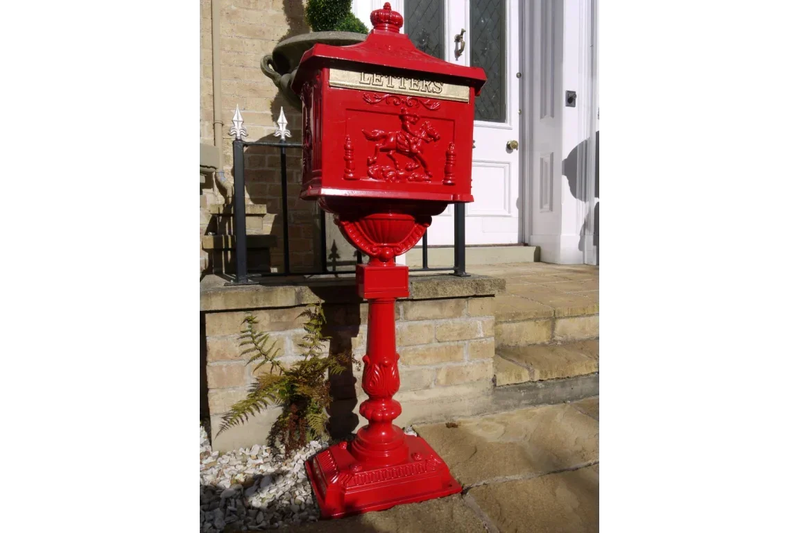 Red cast iron post box with embossed horseman detail on pedestal by stone steps