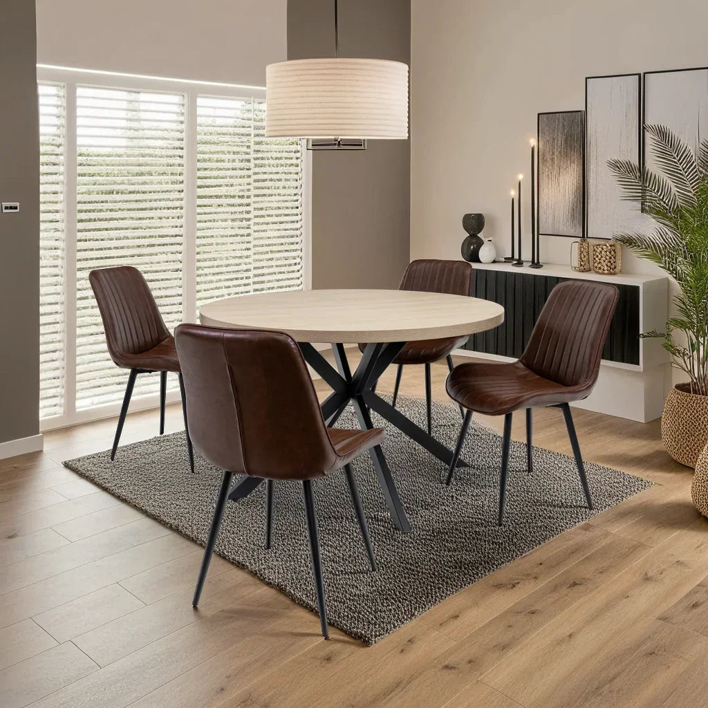 Round dining table with light wood top and four brown leather chairs on a textured rug