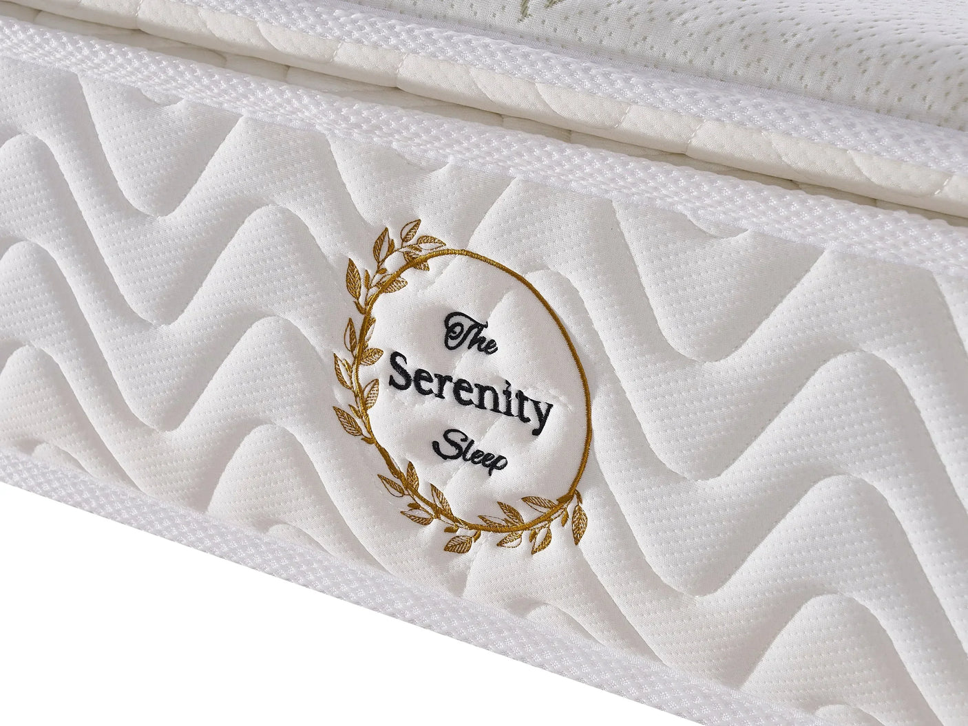 Closeup of Serenity Sleep mattress with quilted white fabric and embroidered gold wreath detail