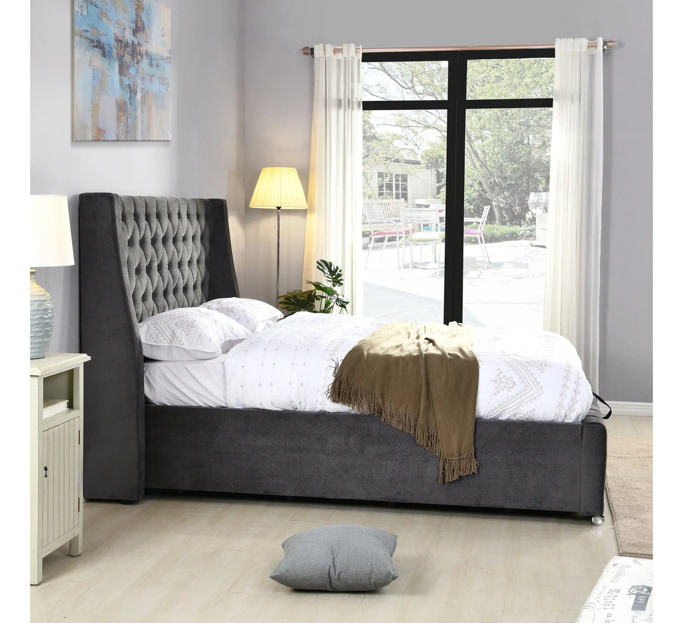 Grey upholstered bed with tufted headboard in bright bedroom with window and floor lamp
