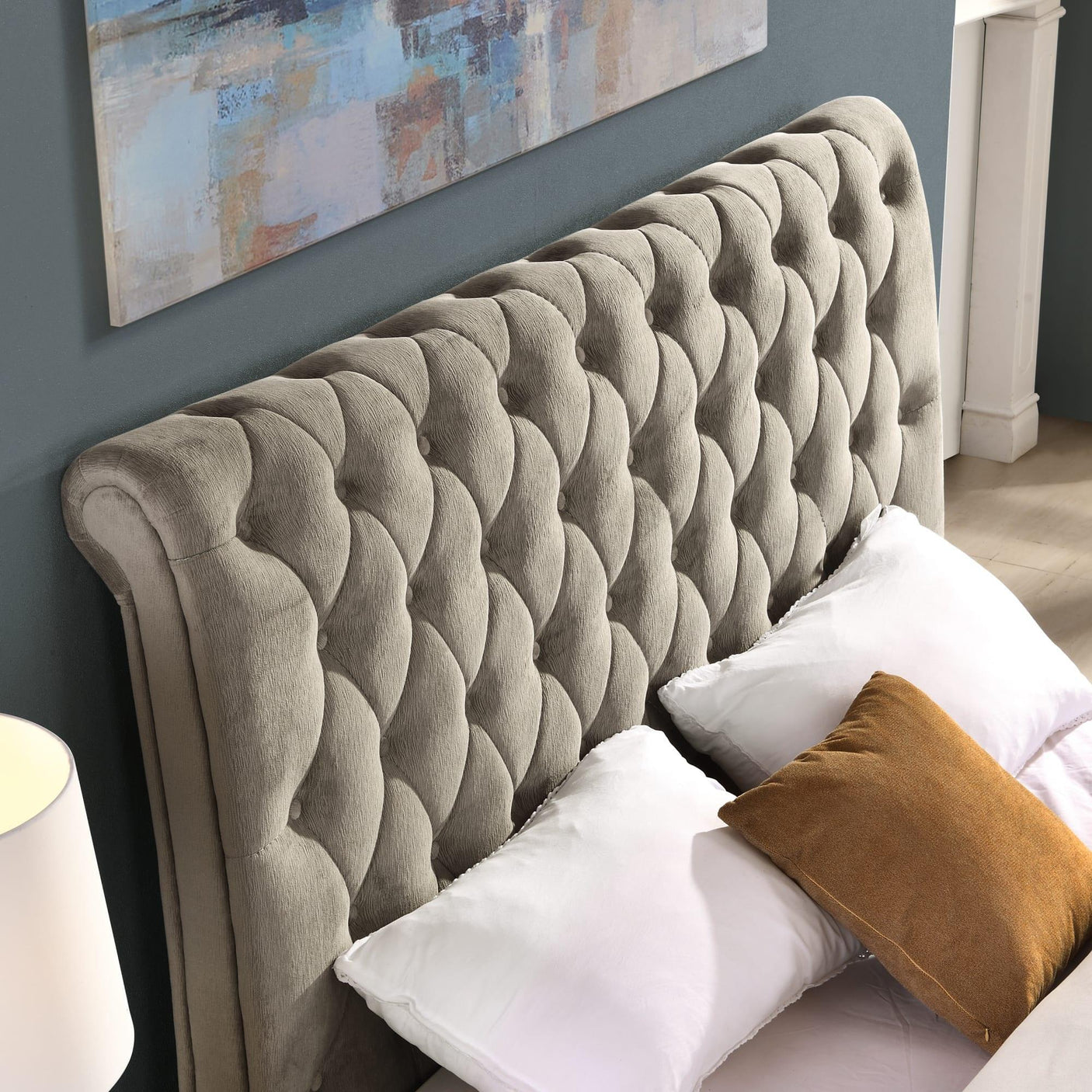 Grey upholstered bed with deep buttoned headboard and white pillows against blue wall