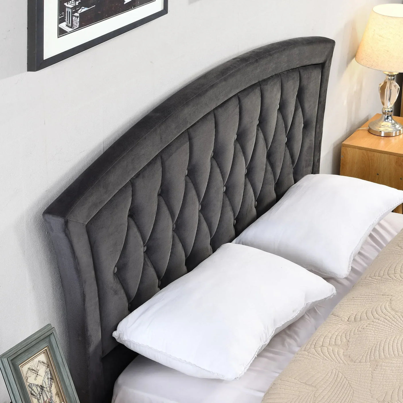 Charcoal grey upholstered bed headboard with diamond tufting beside pillows and lamp