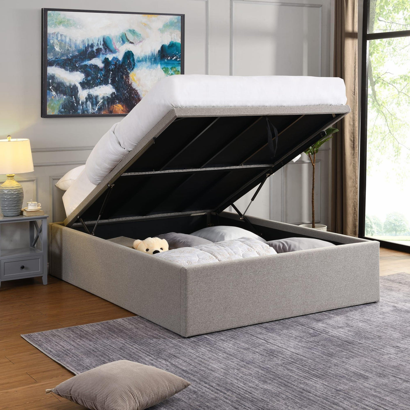 Grey fabric ottoman storage bed frame open, showing bedding and teddy bear inside