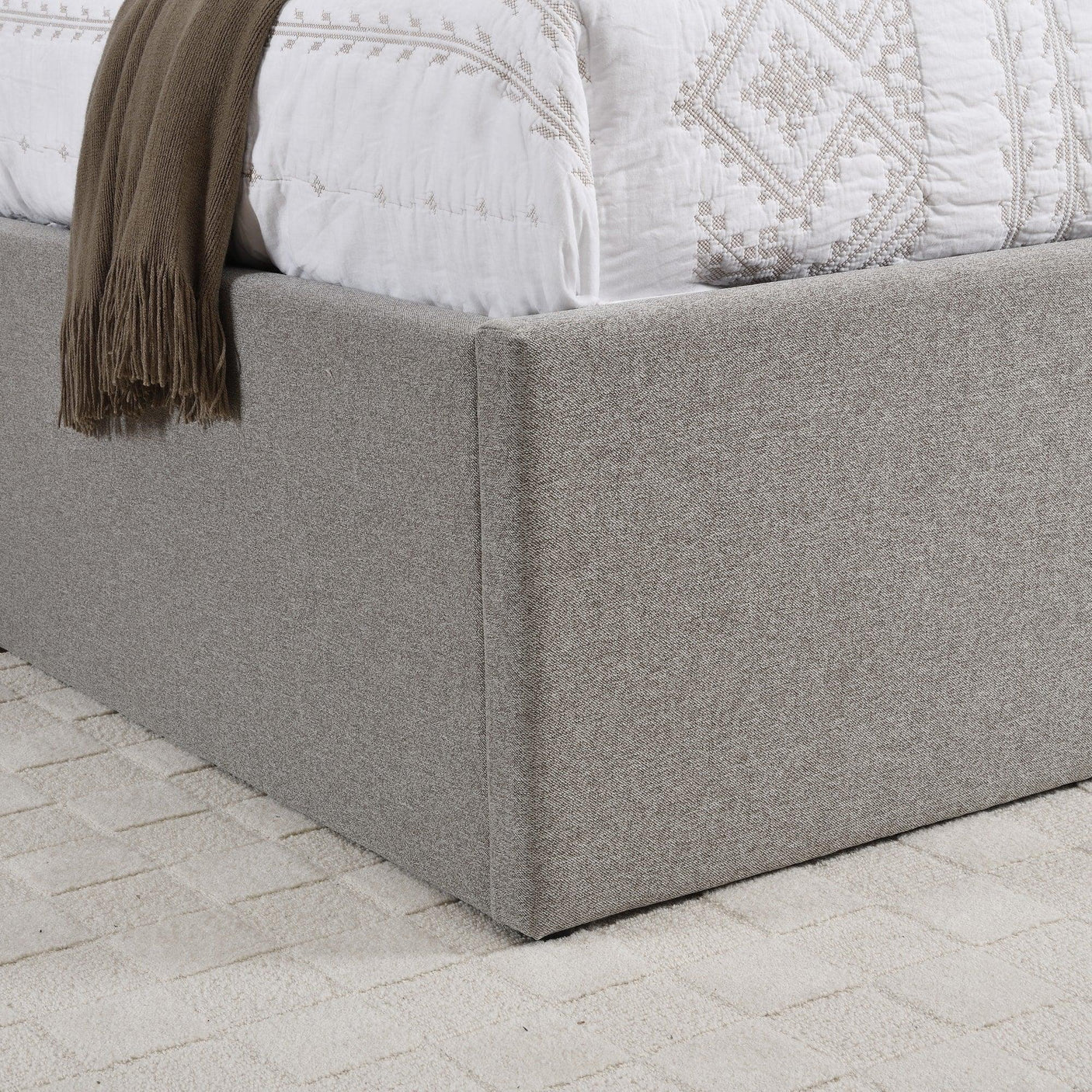 Close up of grey upholstered bed base with textured fabric on cream carpet