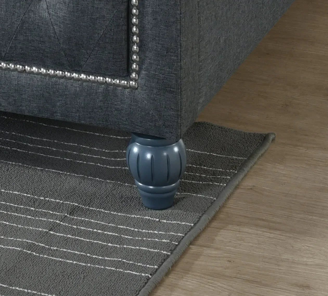 Grey fabric sofa corner with decorative studded trim and turned wooden leg on rug
