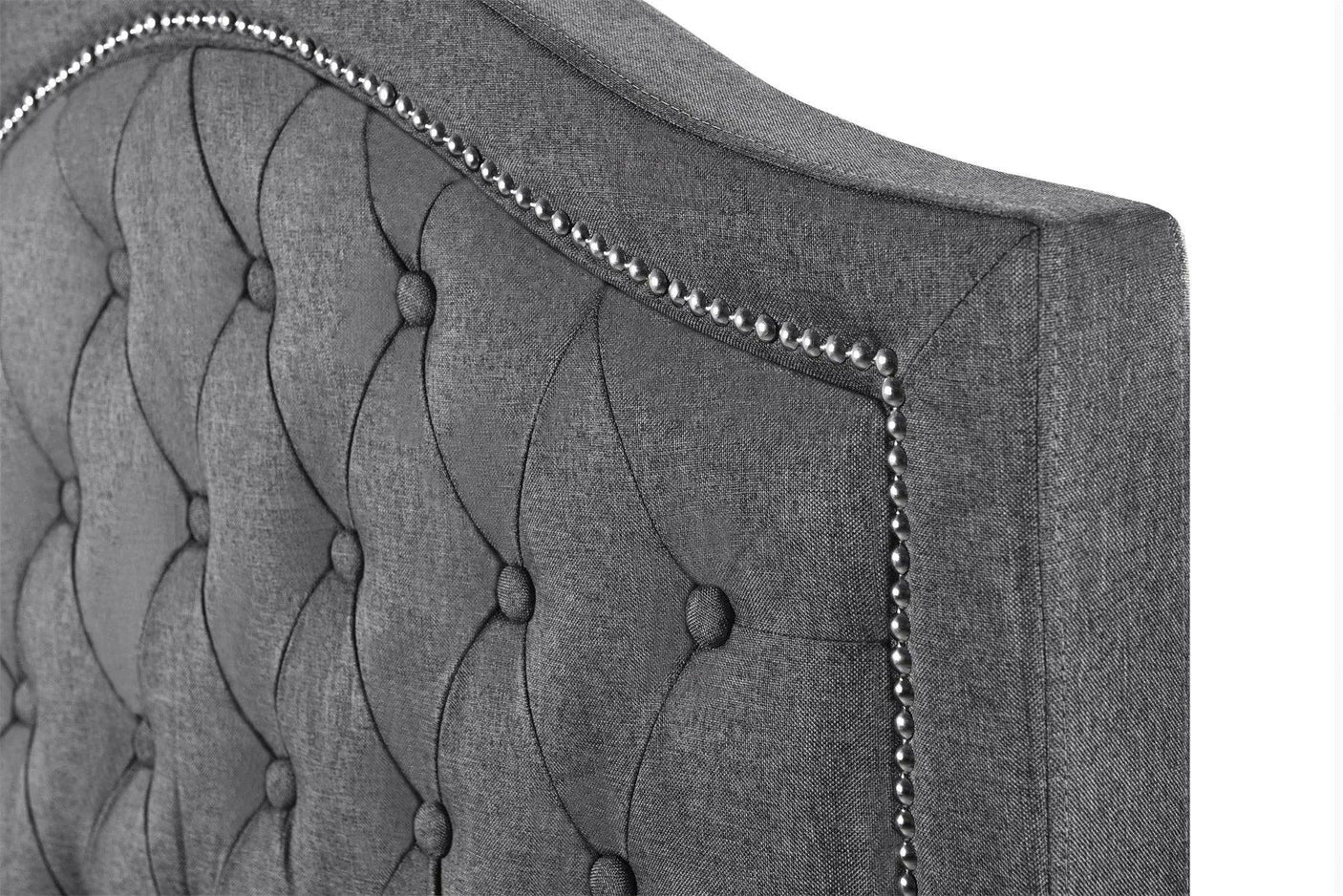 Grey fabric bed headboard with button tufting and studded trim, close-up view