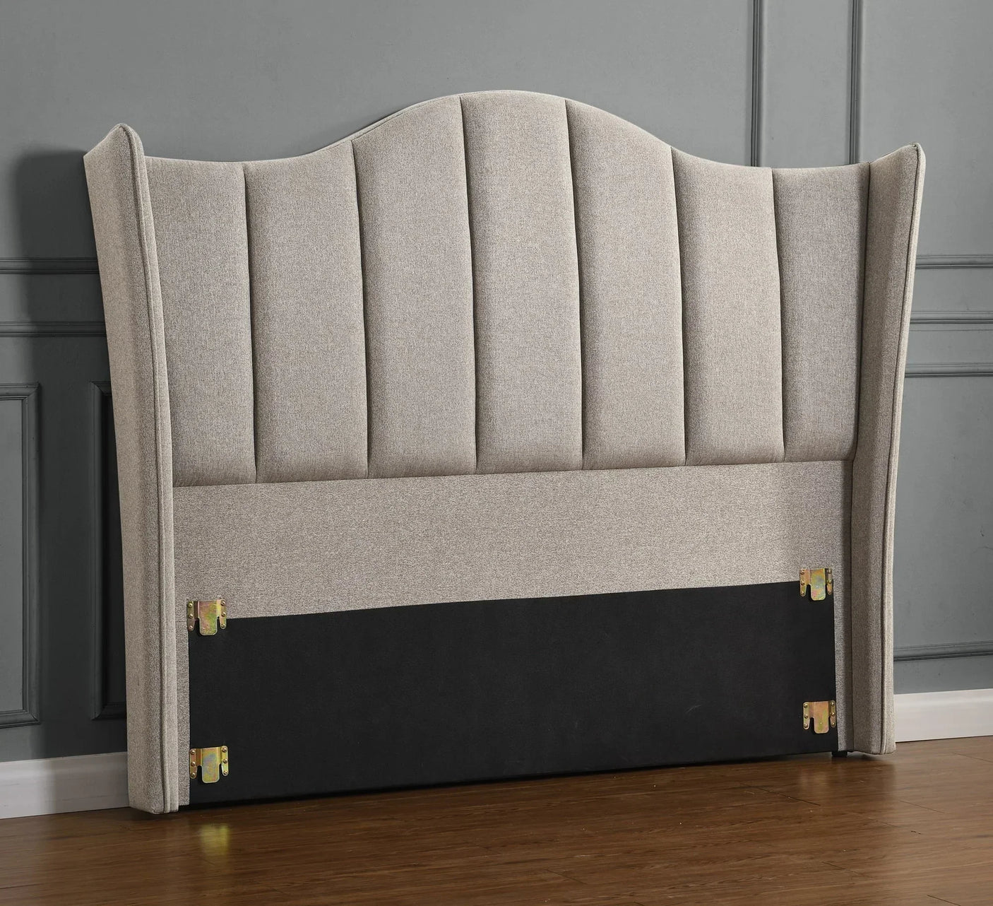 Beige upholstered headboard with vertical panel design against grey wall on wooden floor