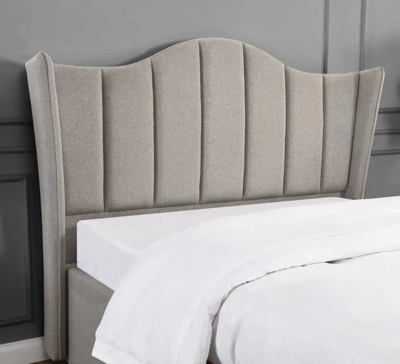 Beige upholstered bed with tall wingback headboard and white bedding against grey wall