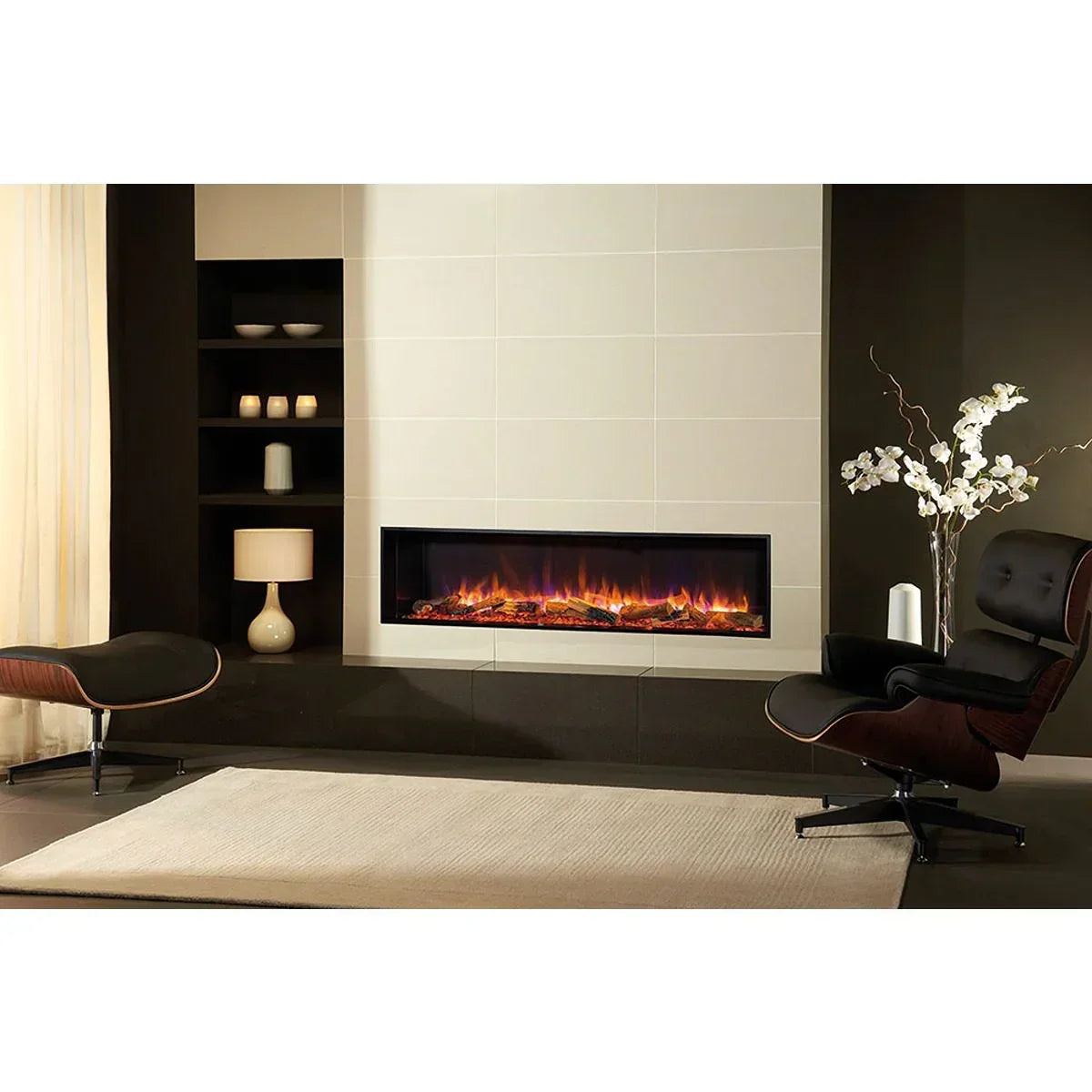 Modern electric fireplace with black trim set in beige tiled wall, lounge chair and shelving nearby