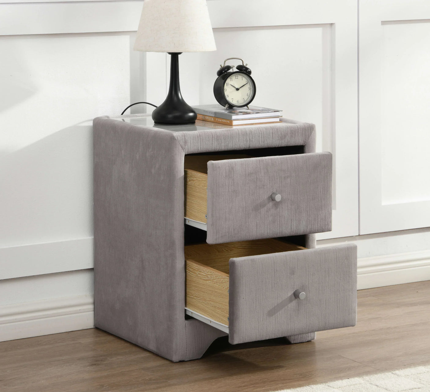 Grey fabric bedside table with two open drawers beside white wall