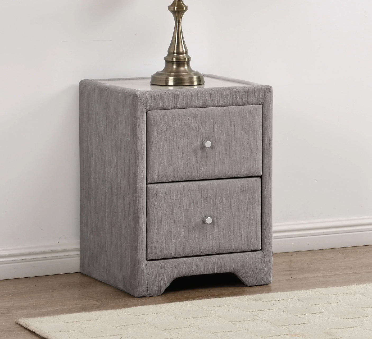 Grey fabric bedside table with two drawers and metal knobs on wooden floor