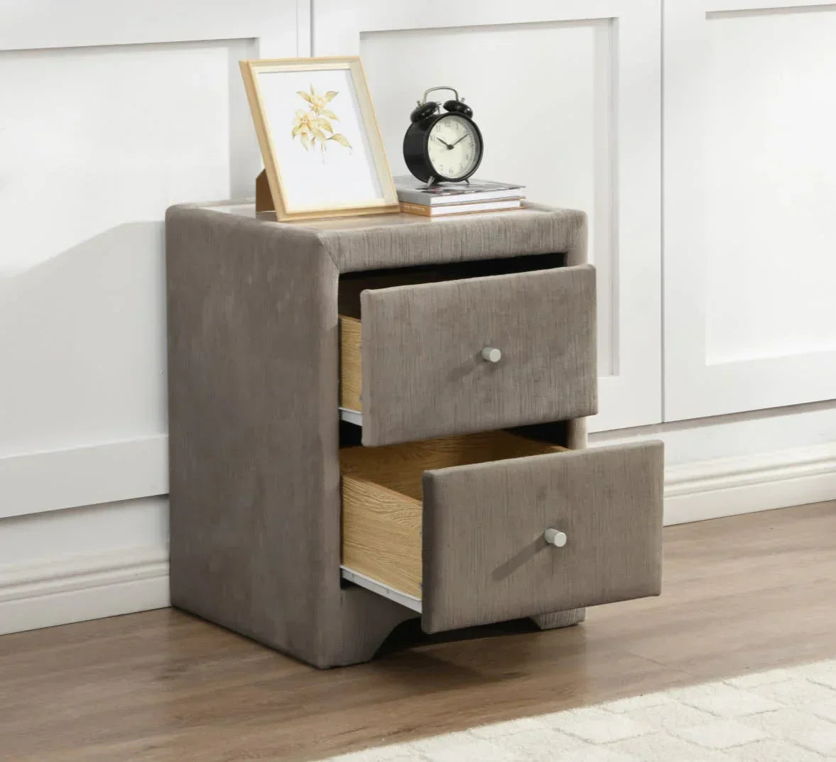 Grey upholstered bedside table with two open drawers, clock and framed print on top