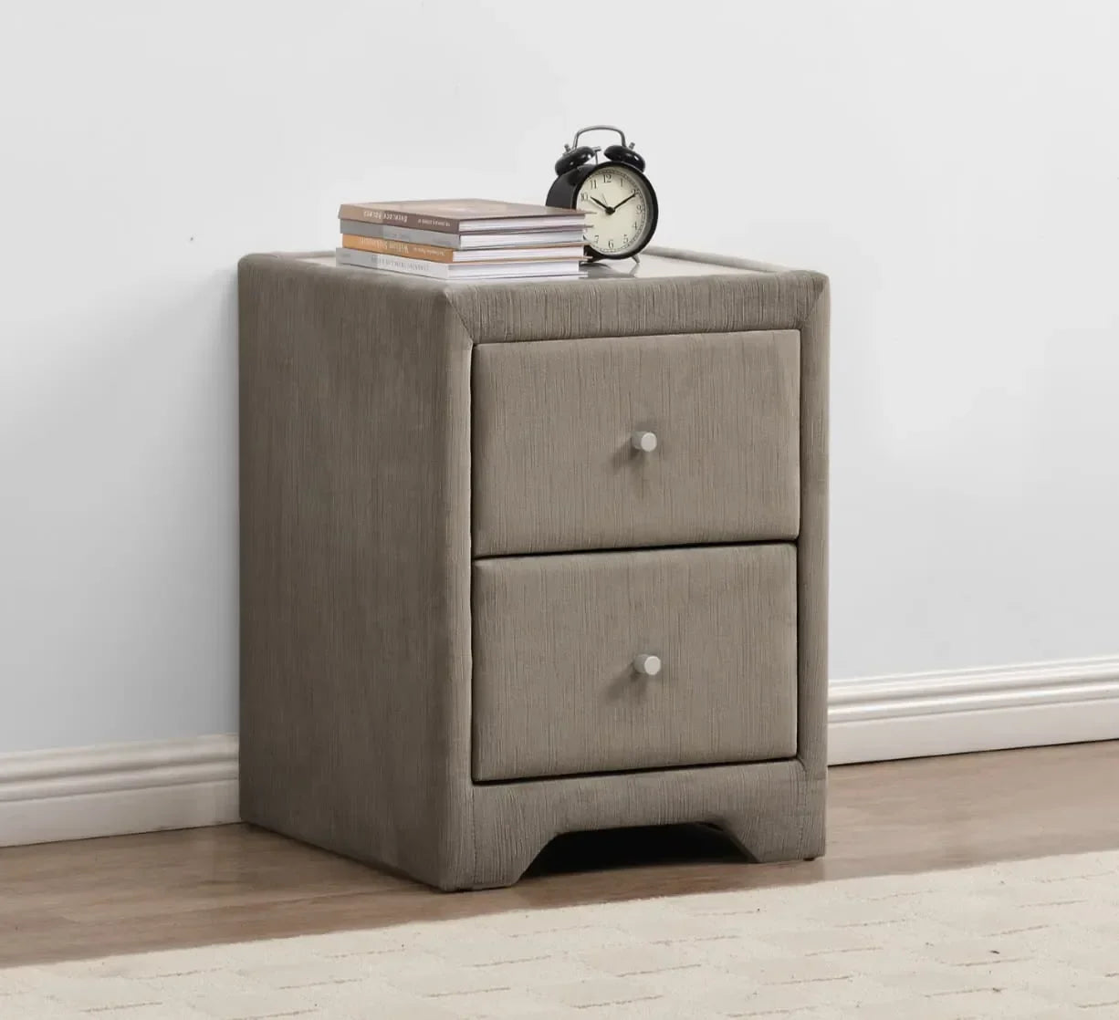Grey fabric bedside table with two drawers, books, and alarm clock on top