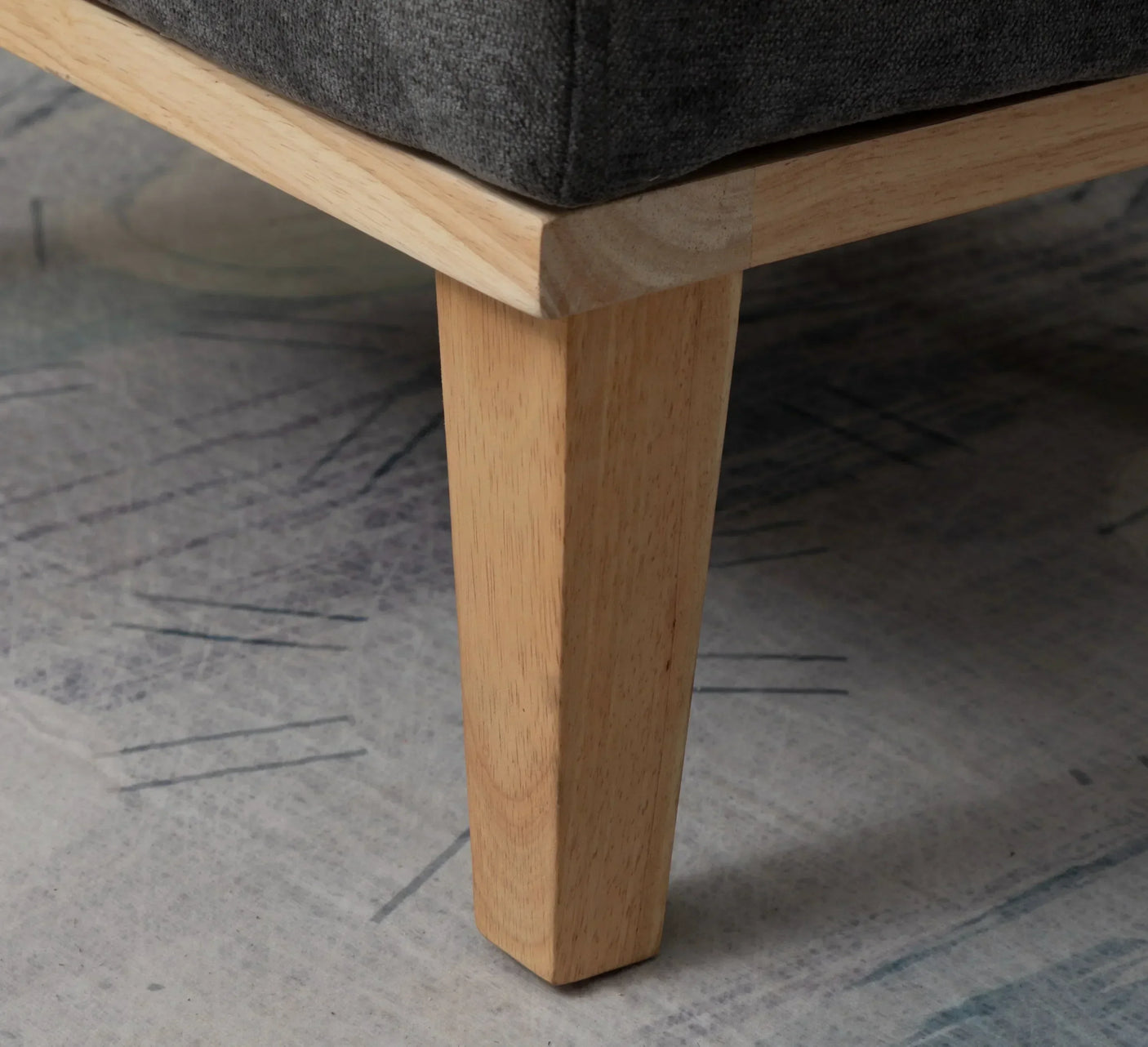 Light wood furniture leg supporting dark grey fabric sofa on patterned rug